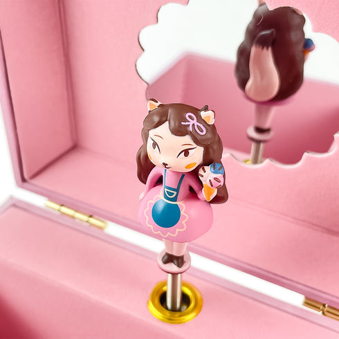 猫の女の子のお人形は、ピンク色のワンピースと青いエプロンをつけています。左手にはチョコチップがかかったトリプルのアイスクリームを持っています。