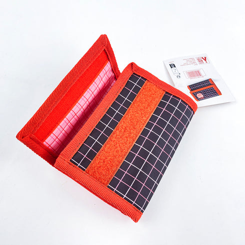 財布のマジックテープを開けたところです。生地は黒に窓枠格子で、赤いバイピングが施されています。マジックテープも赤色です。